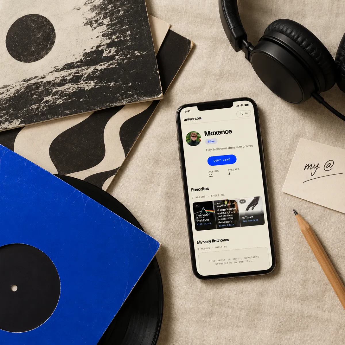 Vue de dessus : un téléphone affiche le profil de @Max parmi des vinyles et un casque